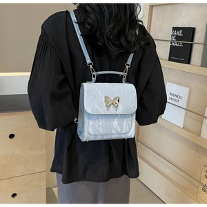 Détail du sac à dos en cuir verni bleu clair avec décoration papillon en métal argenté