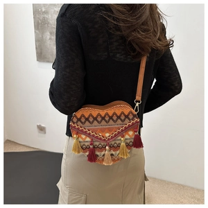 Detail of a woven heart-shaped crossbody bag with tassels and adjustable leather strap