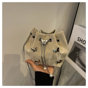 Detail of beige drawstring bucket bag with silver butterfly charms and pearl accents