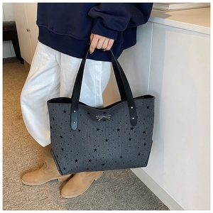 Detail of grey star print tote bag featuring a silver metal bow and leather handles
