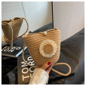 Detail of straw bucket bag with sunflower accent and pearl closure on leather sofa