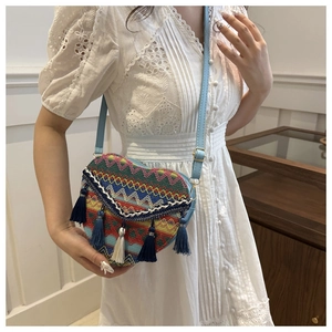 Detail of heart-shaped woven crossbody bag with colorful patterns and tassels on a model