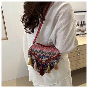 Close-up of heart-shaped woven crossbody bag with colorful tassels on white shirt