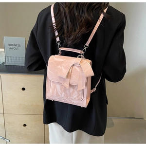 Pink glossy patent leather backpack with large bow detail shown on a black suit jacket