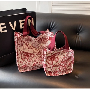 Detail view of two red and white Toile de Jouy pattern canvas tote bags on a leather sofa