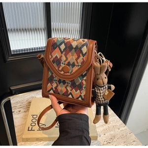 Close-up of woven geometric crossbody phone bag with a plush rabbit charm accessory
