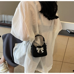 Detail of mini black crossbody bag with silver metal bow and delicate chain strap