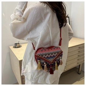 Detail view of a heart-shaped woven crossbody bag with colorful tassels and red strap