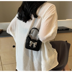 Detail of a mini black crossbody bag with large silver bow and fine metal chain strap