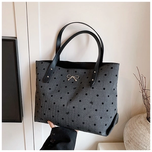 Detailed view of gray tote bag featuring black polka dots and silver metal bow ornament