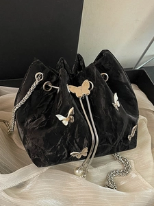 Black bucket bag with butterfly accents and silver chain strap on white silk background