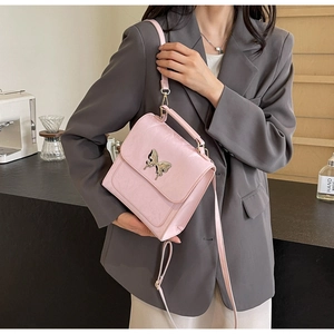 Sac à main en cuir rose avec papillon argenté porté en bandoulière dans un café