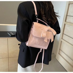 Detail of light pink bow backpack with pleated texture worn over a black blazer