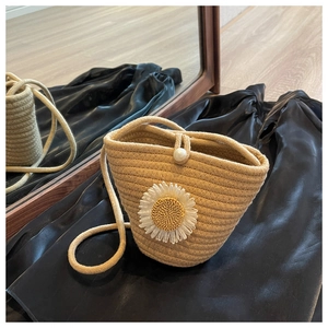 Detail of handmade woven bucket bag with sunflower accent and pearl closure on satin background