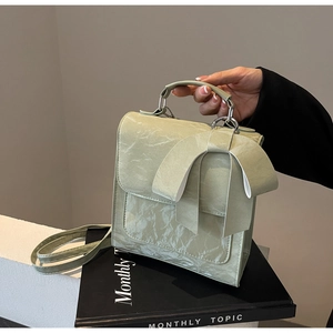 Detailed view of pale green handbag featuring a large bow and elegant pleated texture