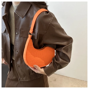 Sac hobo demi-lune orange vif à motif crocodile porté avec une veste en cuir