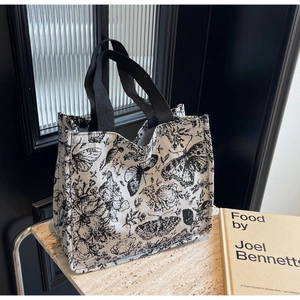 Detailed view of cream canvas tote bag with black butterfly floral prints and woven straps