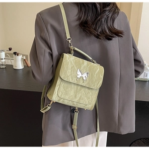 Détail du sac à dos en cuir plissé vert clair avec papillon argenté dans un café urbain