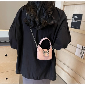 Pink mini crossbody bag with silver bow accent shown on model for size perspective