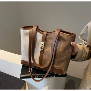Detail view of canvas tote bag with brown leather trim and metal twist lock on a white step