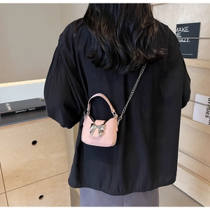 Detailed view of mini pink suede crossbody bag with metallic bow and chain strap