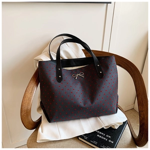Detail of black tote bag featuring red heart patterns and silver metal bow ornament