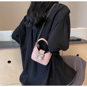 Close-up of a pink mini crossbody bag with a silver metal bow and delicate chain strap