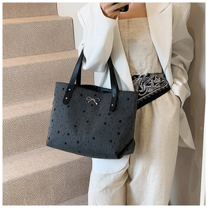Detail of dark gray star pattern tote bag with silver bow charm on stylish woman