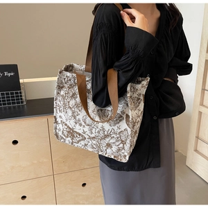 Detail of a beige knit tote bag with brown floral patterns worn over the shoulder