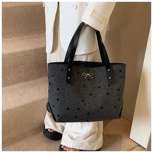 Detail of grey canvas tote bag with black star patterns and gold bow decoration