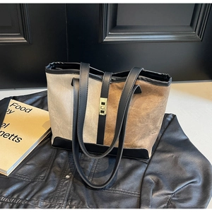 Detail of two-tone tote bag featuring beige canvas, black leather straps and gold buckle