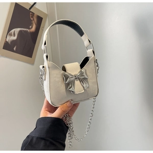 Detail of a creamy white mini bag featuring a large silver metal bow and chain strap