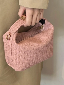 Pink woven handbag with golden metal hardware held by a model in khaki outfit