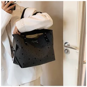 Detailed view of dark grey tote bag with black star prints and silver bow on model