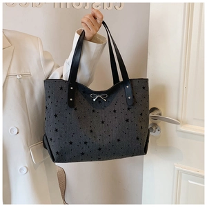 Detail of dark grey tote bag with black star patterns and a metal bow ornament