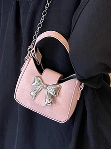 Pink mini crossbody bag with silver bow accent and chain strap worn by a model