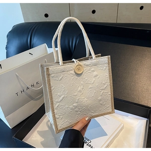 Close-up of linen tote bag with 3D rose texture and wooden button closure in hand