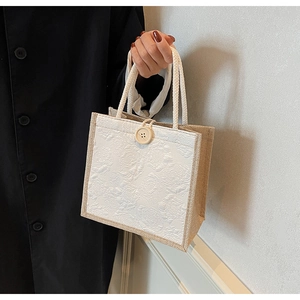 Detail of white embossed floral tote bag with linen sides and wooden button closure