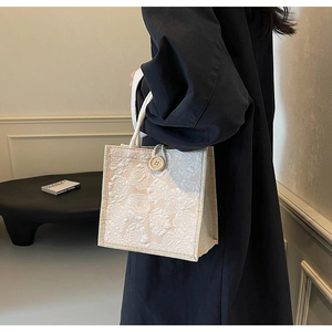 Detail showing off-white jacquard tote bag texture with elegant floral relief pattern