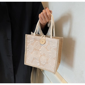 Detail of floral embossed linen handbag with woven rope handle and wooden button closure