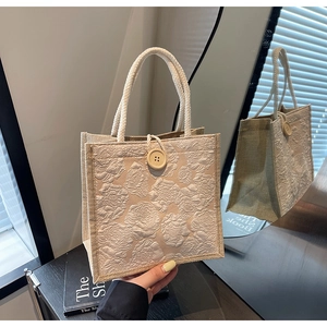 Detailed view of beige linen tote with embossed flowers and woven rope handles