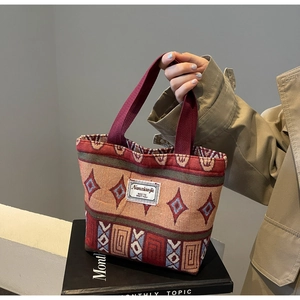 Detail of hand-woven canvas bucket bag showing ethnic patterns and burgundy handles