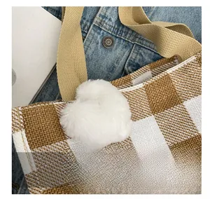 Detail of plaid tote bag featuring a white plush heart charm and khaki strap texture