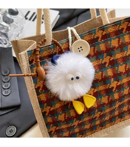 Close-up of cute cartoon plush doll hanging on a linen handbag with checkered pattern