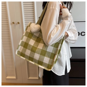 Detail view of large green checkered tote bag with plush heart charm on woven fabric