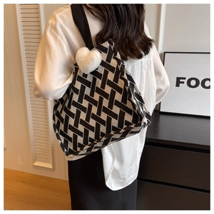 Detail view of a black and white geometric knit tote bag with a white plush heart charm