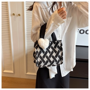 Detail of checkered knit tote bag with black canvas straps and a white plush heart charm