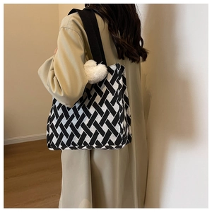 Black and white geometric woven tote bag with wide strap and white plush heart pendant