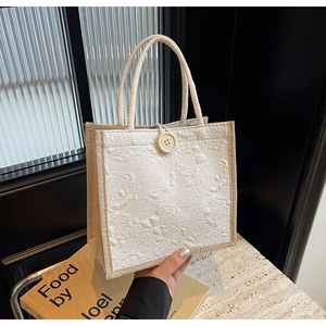 Detail of white linen tote bag with 3D floral texture and wooden button closure