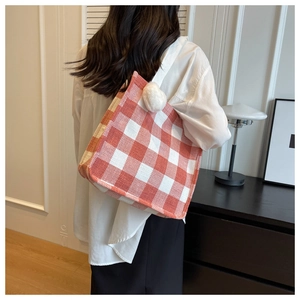 Détail d'un sac cabas tissé à carreaux orange et blanc avec un pompon en peluche blanche